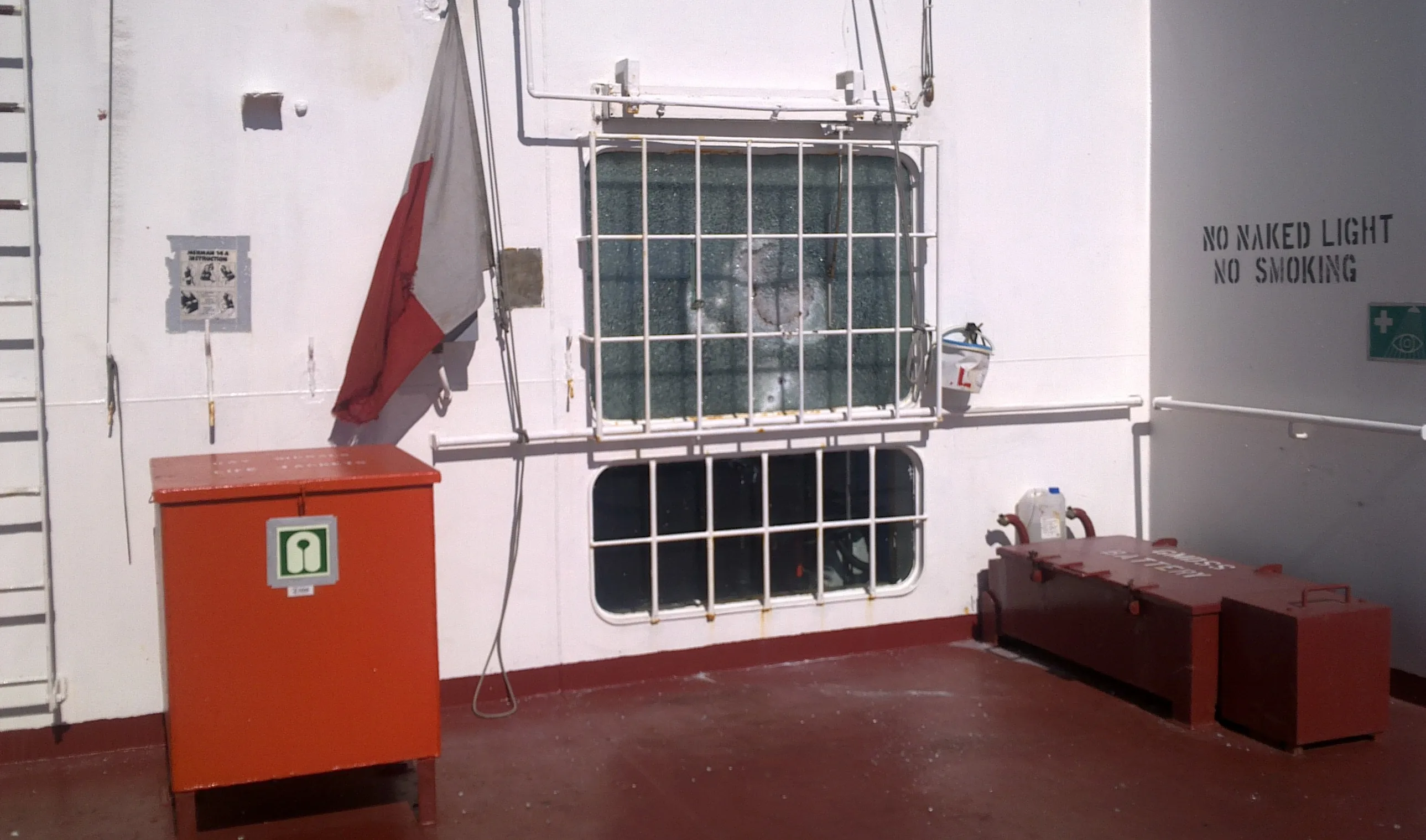 Vessel bridge exterior showing windows hit by small arms fire — glass shattered but held in place by anti-blast film