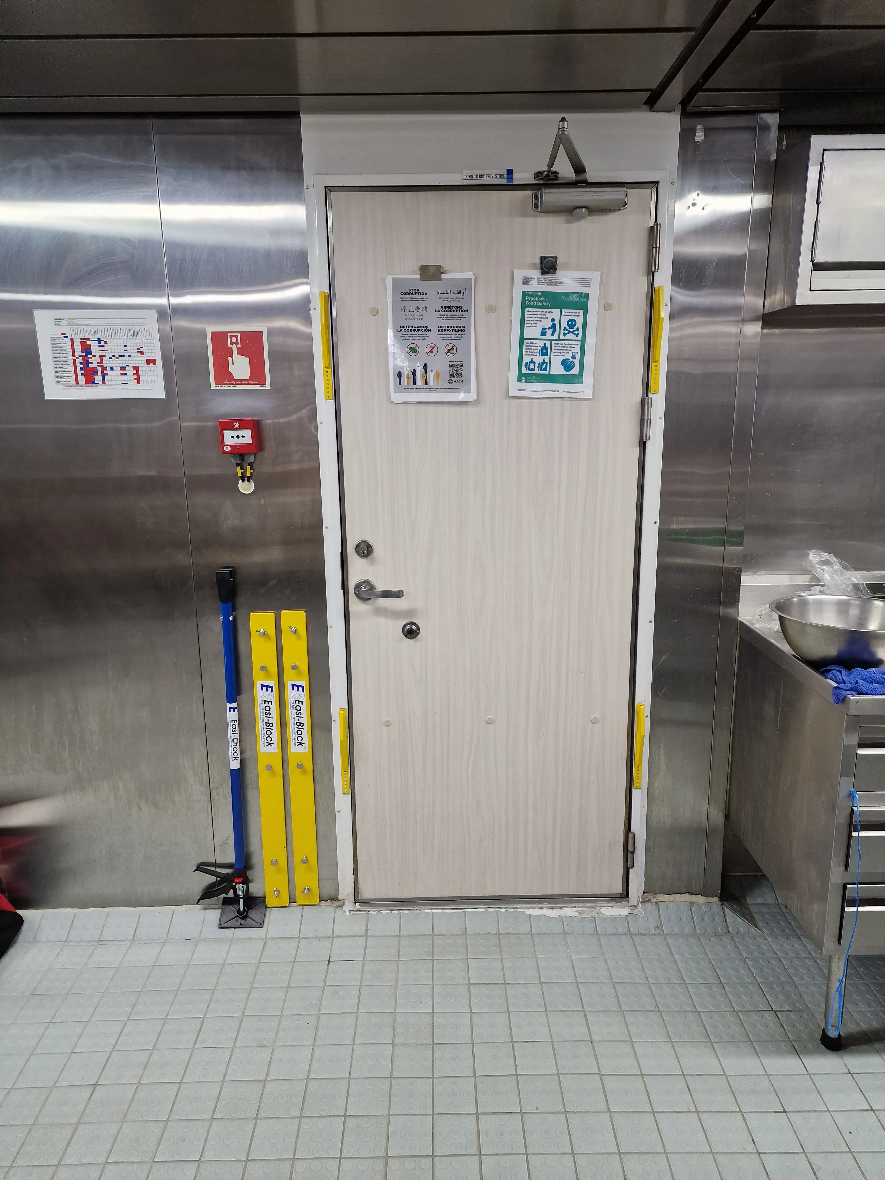 Easi-Block door securing bars disengaged, leaning against the wall beside a ship galley door